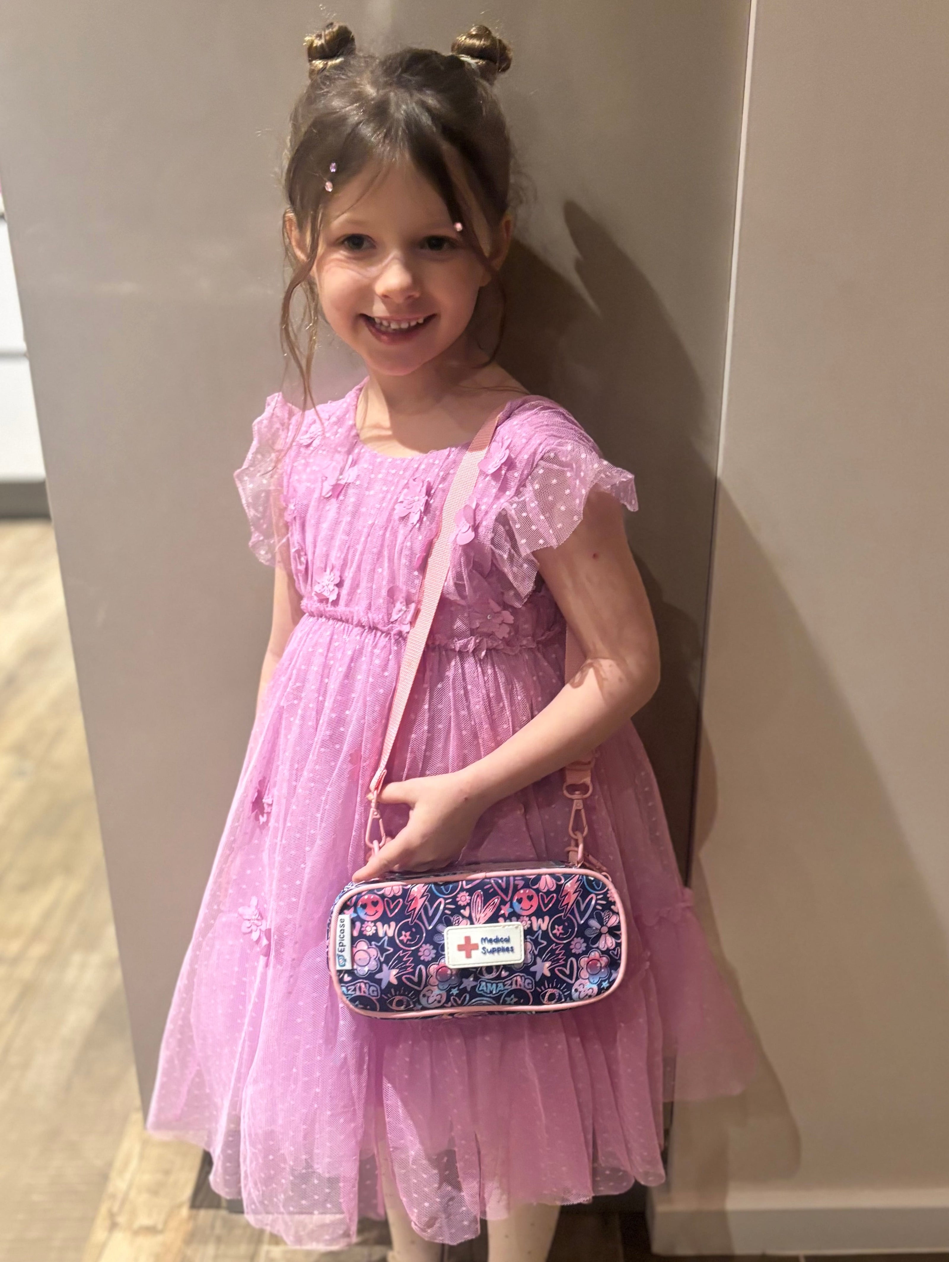 girl standing against a wall in a pink dress holding a purple Epicase