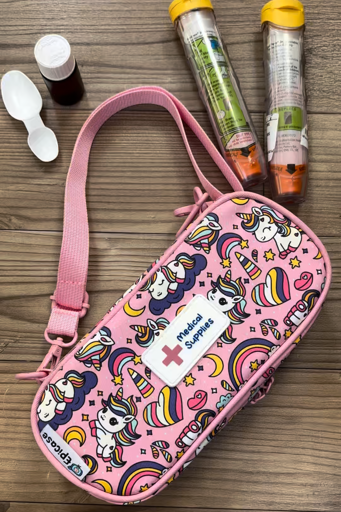 Pink Epicase on wooden table with small medicine bottle, medicine spoon and two epipens
